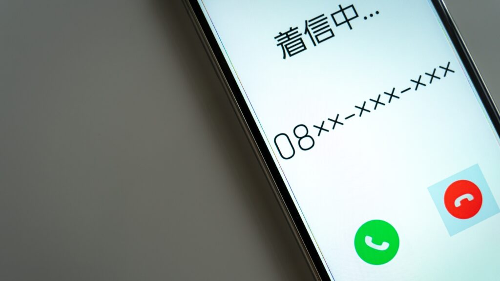 スマートフォンの画面に表示された「着信中...」の文字と架空の電話番号、緑の通話ボタンと赤の終了ボタン