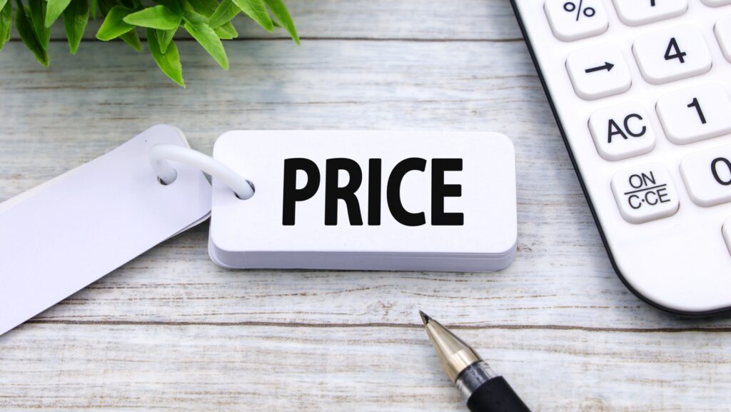 木目調のテーブルの上に置かれた、「PRICE」と書かれた白い単語帳と、右側にある白い電卓、手前のボールペン